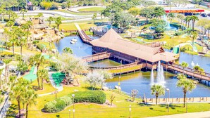 A large building with a distinctive roof, surrounded by a water feature and palm trees. - Stunning beachfront condo with water views, pool, hot tub, & sauna (Panama City Beach)