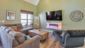 A living room with a brown leather sofa, a black armchair, a wooden coffee table, and a flat-screen TV mounted on the wall. - Blue Ridge Retreat: 1 Mi to Kingwood Golf (Clayton)