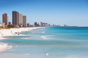 Uma praia com águas turquesa cristalinas e uma fileira de edifícios altos ao fundo.