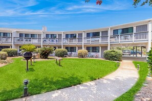 A multi-story building with balconies, a well-maintained lawn, and a paved pathway. - Beautiful coastal studio condo with pool (Santa Rosa Beach)
