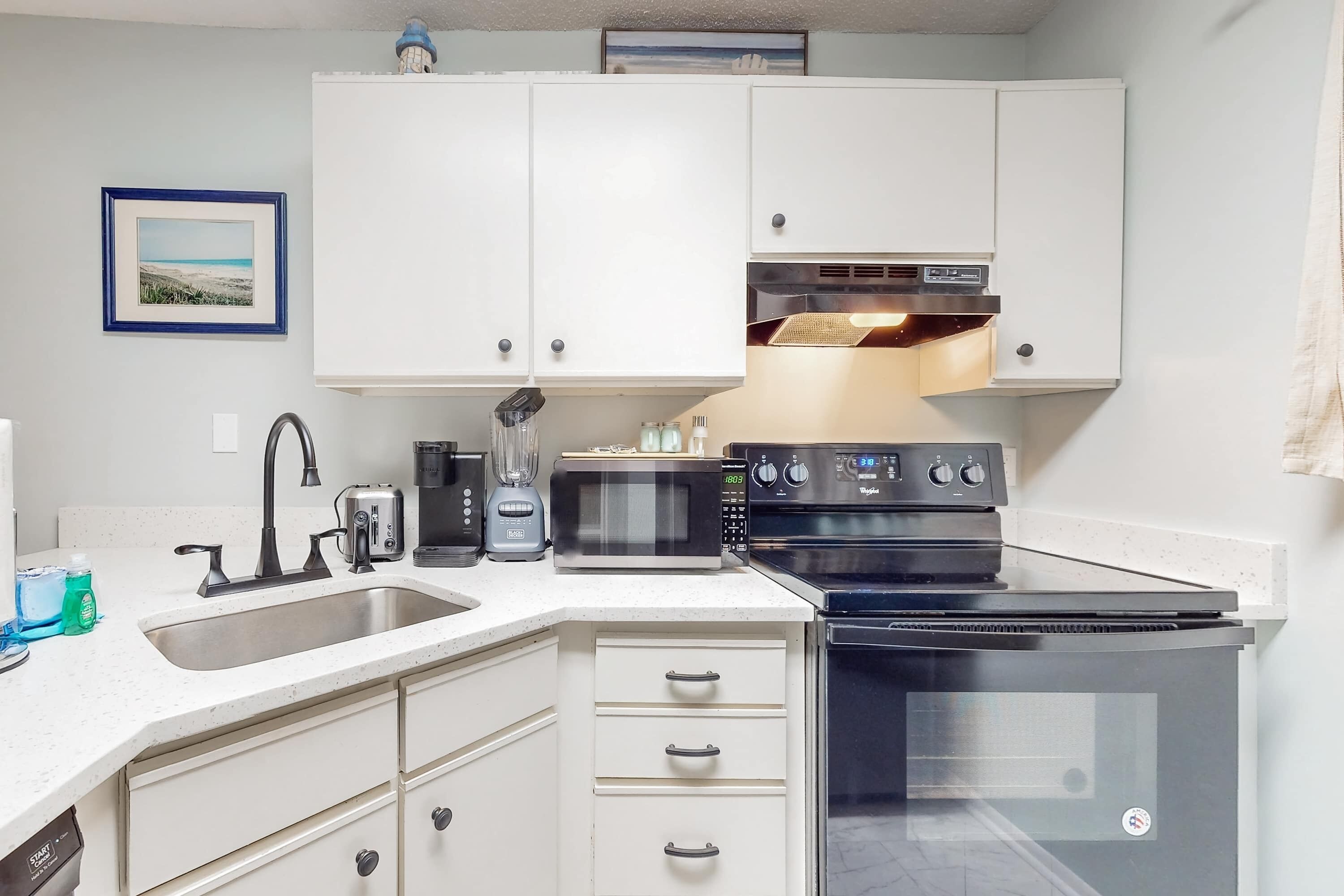 A modern kitchen with white cabinets, a stainless steel sink, a microwave, a stove, and a dishwasher.