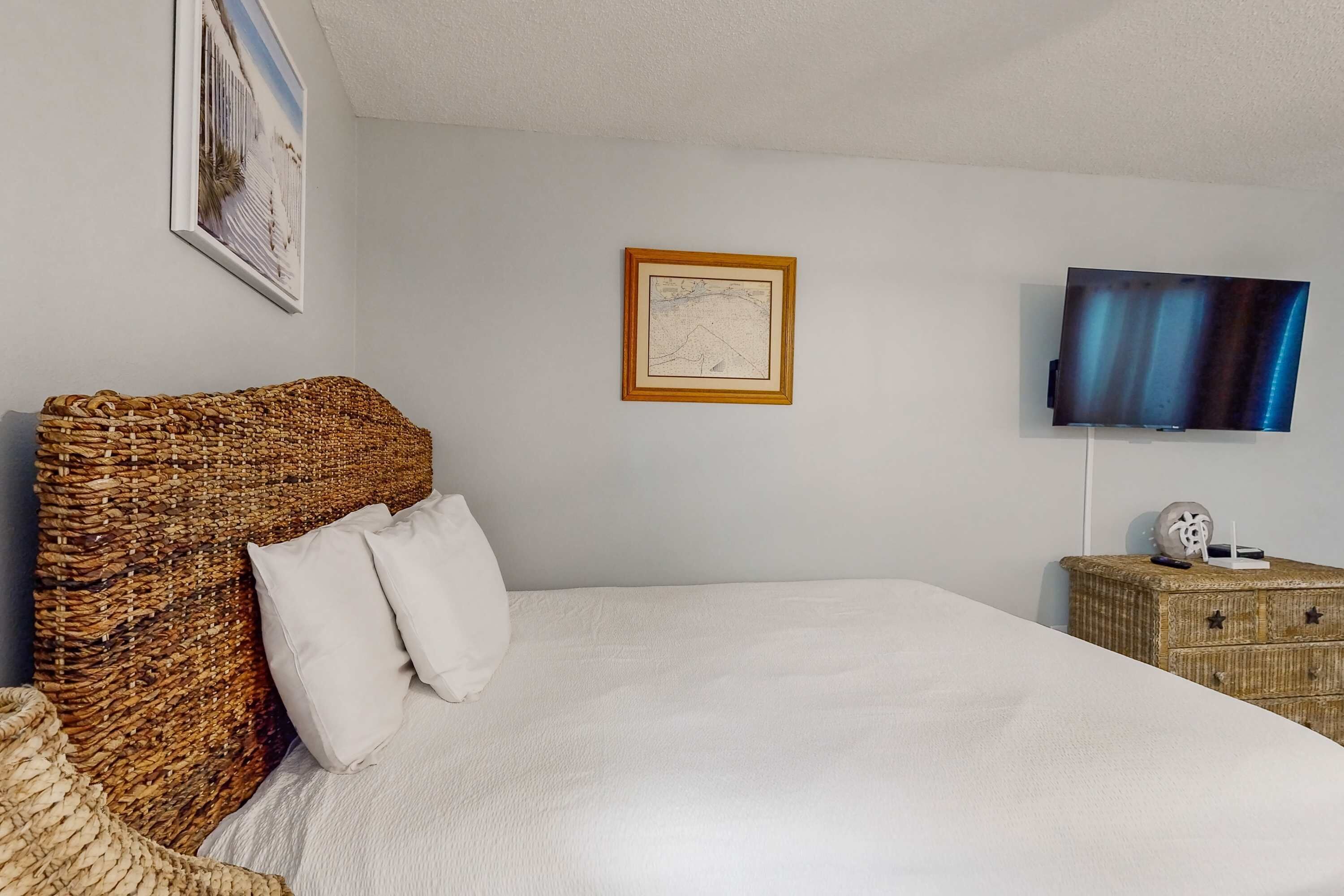 A bedroom with a large bed, a television, a framed picture, and a wicker headboard.