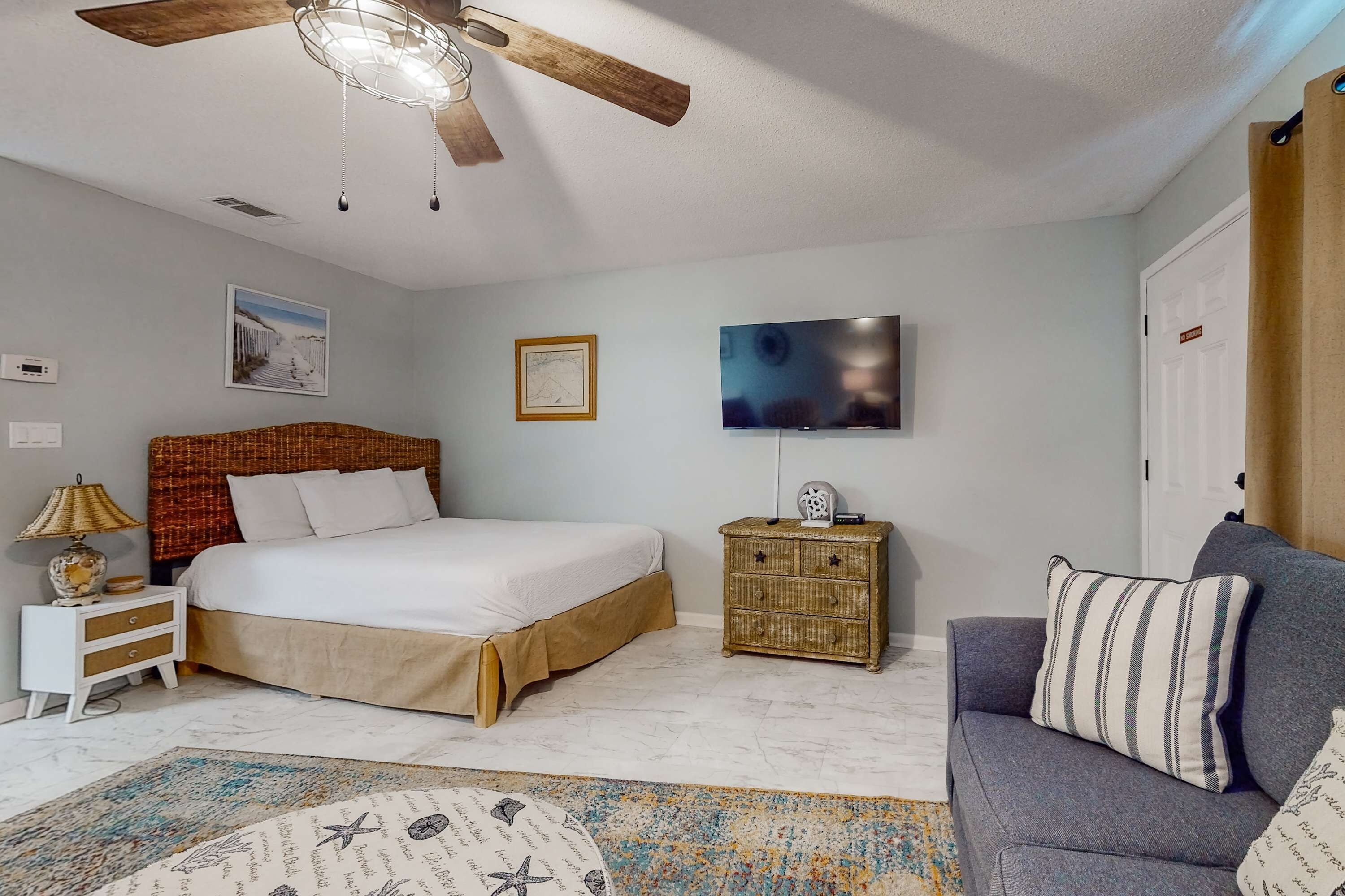 Une chambre à coucher avec un lit, une table de chevet, un téléviseur, un ventilateur de plafond et un canapé.