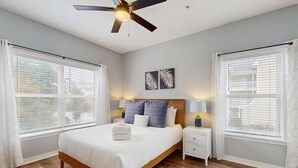 A bedroom with a wooden bed, white bedding, two wall-mounted lamps, and a ceiling fan. - Pool-view condo with private balcony, washer and dryer, Wifi, 2 bikes included (Santa Rosa Beach)
