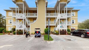A multi-story building with balconies, a parking lot, and a golf cart. - Pool-view condo with private balcony, washer and dryer, Wifi, 2 bikes included (Santa Rosa Beach)