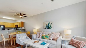 A modern living room with a sofa, coffee table, and dining area. - Pool-view condo with private balcony, washer and dryer, Wifi, 2 bikes included (Santa Rosa Beach)
