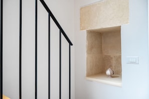Un escalier avec des rampes noires, un mur de couleur beige et une petite étagère sur laquelle est posé un objet décoratif.