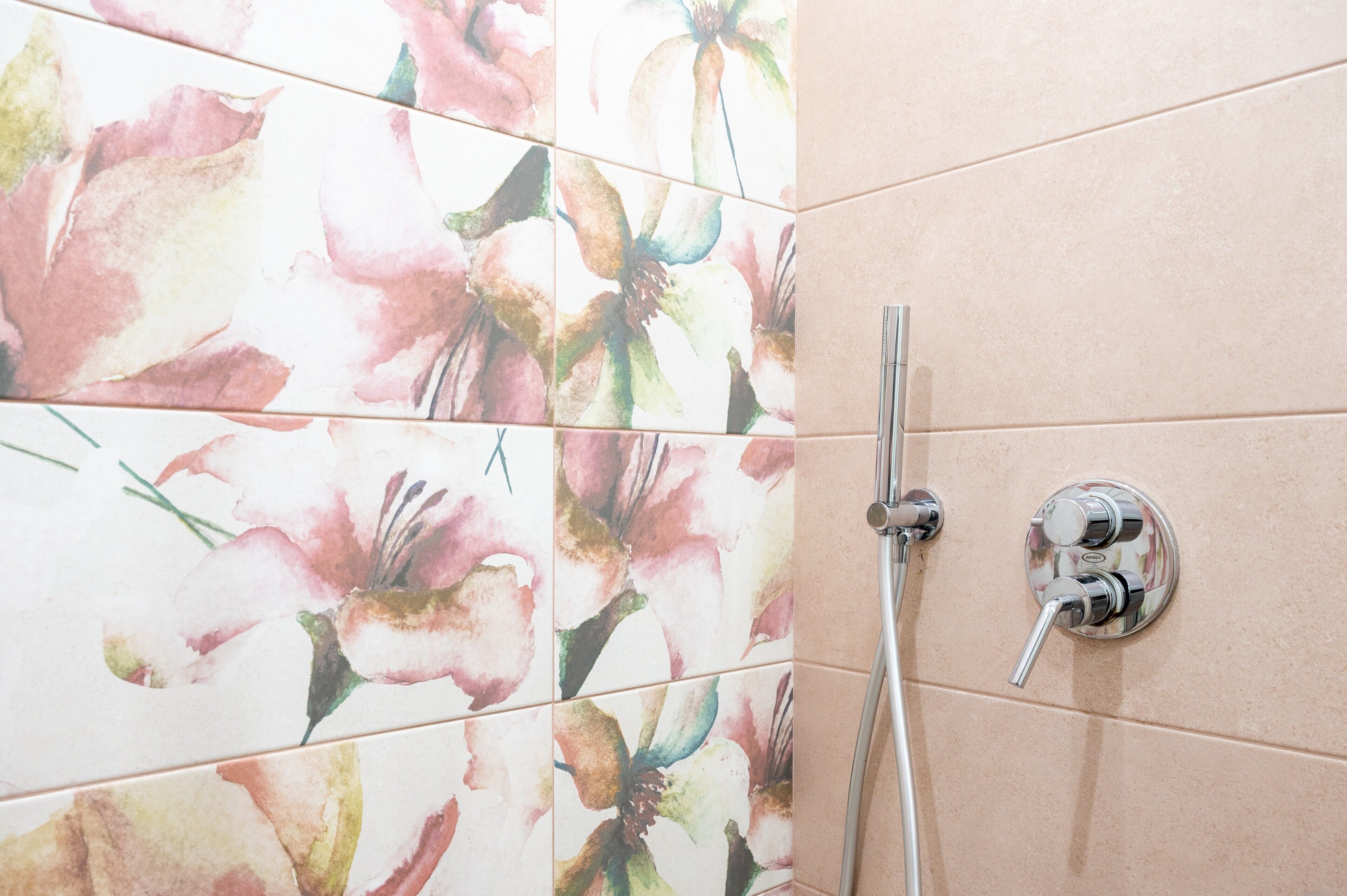 A bathroom with floral tiles, a shower, and a wall-mounted faucet.