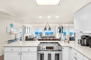 A modern kitchen with a central island, stainless steel appliances, and a view of the ocean. - Waterfront condo with a scenic balcony and AC - pool, gym, and grill access (Panama City Beach)