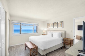 A bedroom with a bed, a bench, a nightstand, a lamp, and framed pictures on the wall. - Waterfront condo with a scenic balcony and AC - pool, gym, and grill access (Panama City Beach)