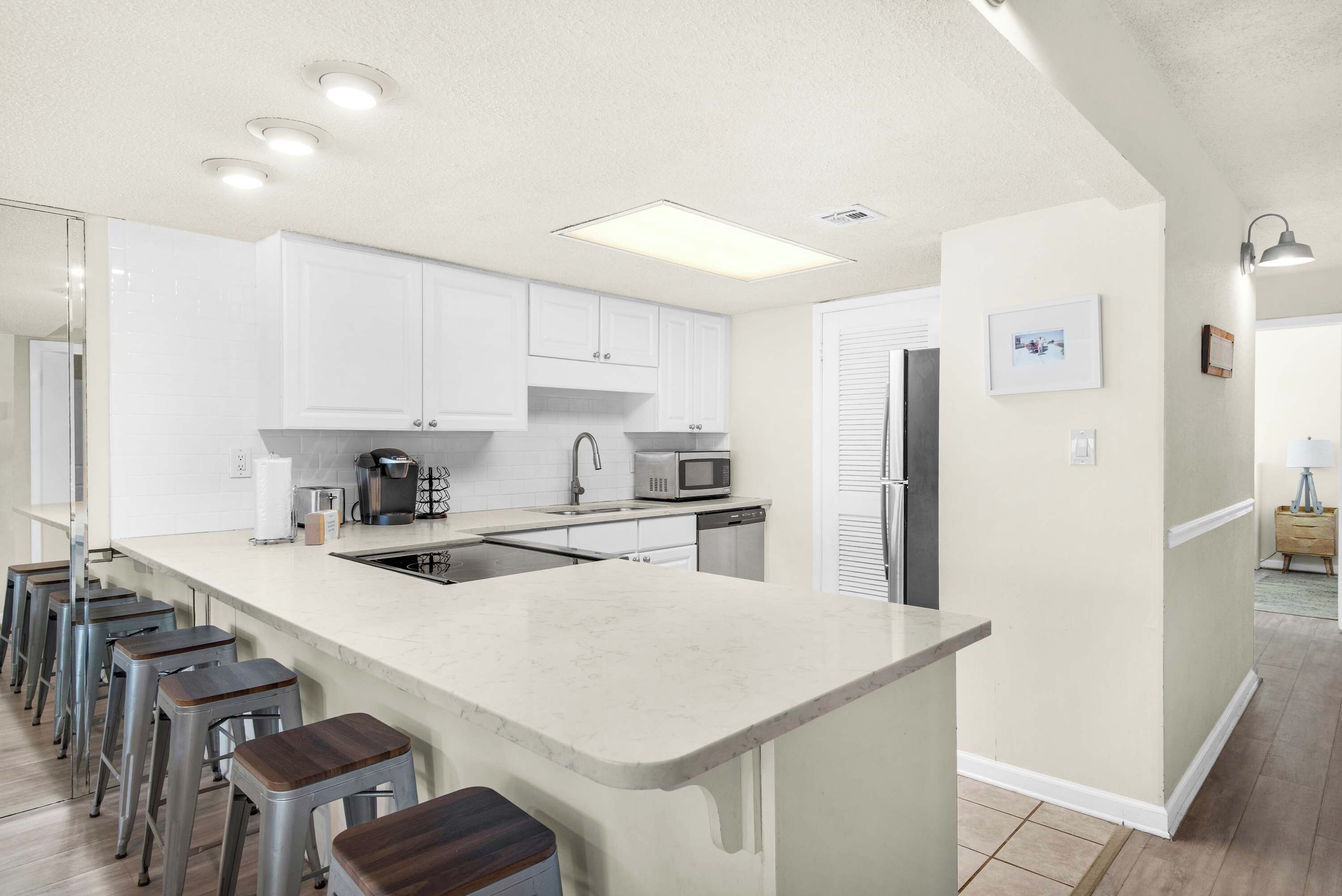 A modern kitchen with white cabinets, a central island, bar stools, and stainless steel appliances.