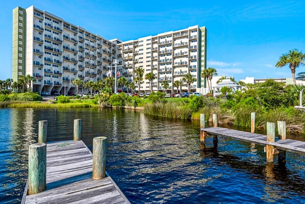 Un hotel de varios pisos con balcones, un muelle que se adentra en el agua y vegetación circundante.