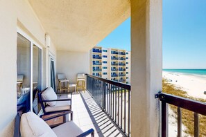 A balcony with a view of the beach and a building in the background. - Waterfront condo with a scenic balcony and AC - pool, gym, and grill access (Panama City Beach)