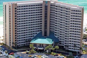 A high-rise hotel with multiple balconies, a central green-roofed building, and a parking lot with cars. - 17th-floor Gulf-front condo with indoor & outdoor pools, hot tub & on-site dining (Destin)