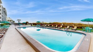 A swimming pool with lounge chairs and umbrellas, surrounded by a fence and a building. - Oceanfront condo with shared pool, resort amenities, and private washer/dryer (Panama City Beach)