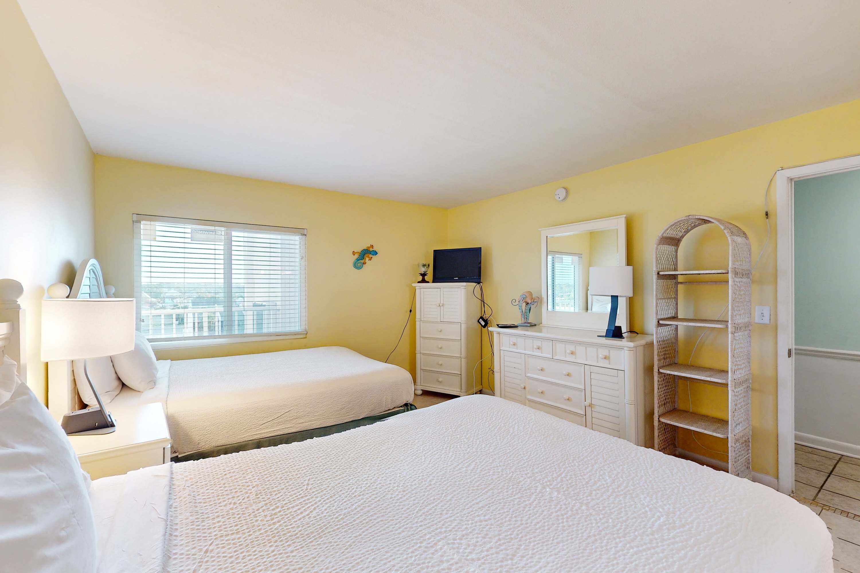 A hotel room with two beds, a dresser, a TV, and a window with blinds.