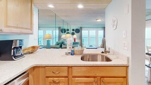 A kitchen with wooden cabinets, a stainless steel sink, and a coffee maker. - Oceanfront condo with shared pool, resort amenities, and private washer/dryer (Panama City Beach)