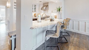 A modern kitchen with white cabinetry, a granite countertop, and a central island with bar stools. - Gorgeous, updated condo with balconies, pool, & great location near 30A (Alys Beach,)