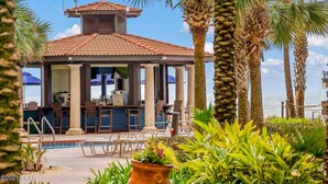 Zona de bar al aire libre con asientos, piscina y palmeras.