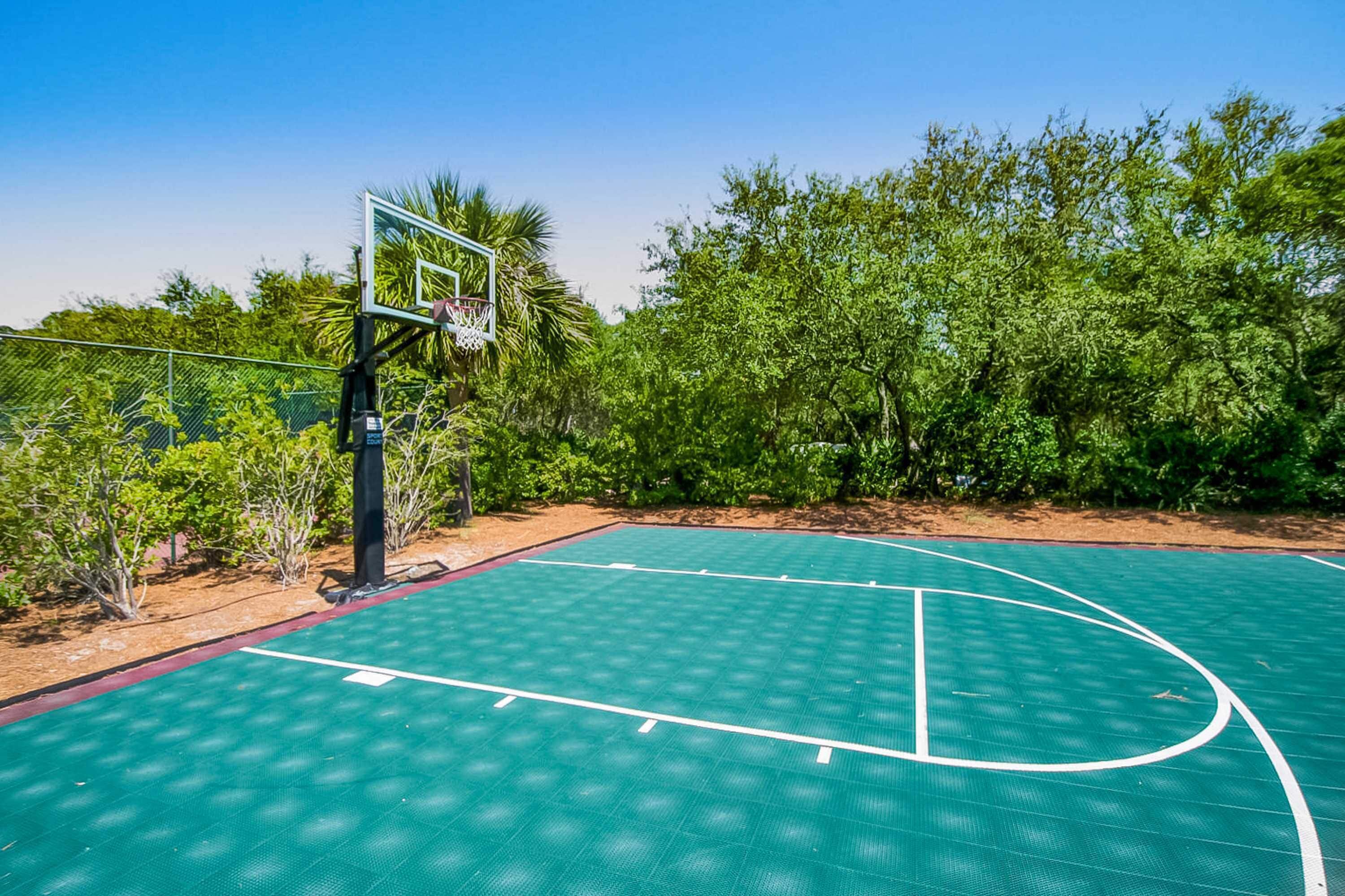 An outdoor basketball court with a green surface, surrounded by trees and a fence.