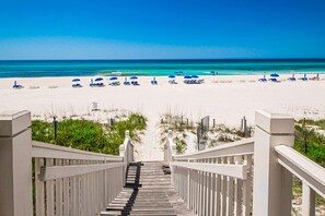 A wooden staircase leading to a beach with white sand and blue umbrellas. - Stunning lake-view condo with private balcony, pools, hot tub, & private beach (Panama City Beach)