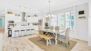 A spacious kitchen with white cabinetry, a central island, bar stools, and a dining table with chairs. - Relaxing getaway outdoor pool access, gym, bikes, central AC, & W&D (Inlet Beach)