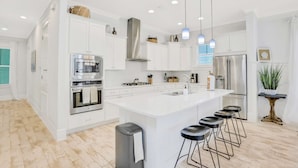 A modern kitchen with white cabinetry, stainless steel appliances, and a central island with bar stools. - Relaxing getaway outdoor pool access, gym, bikes, central AC, & W&D (Inlet Beach)