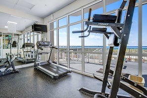 A gym with treadmills, exercise bikes, and weight machines, large windows with a view of a bridge and water. - 7th Floor Gulf-Front Condo w/ Views, Close To Local Restaurants (Navarre Beach)