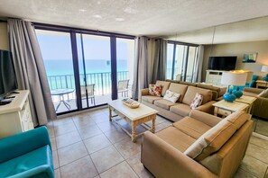 Un salon moderne avec un canapé, une table basse et un téléviseur. La pièce est dotée de grandes fenêtres offrant une vue sur la mer.