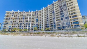 Hotel com vários andares e varandas, situado perto de uma praia.