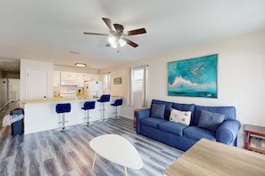 A modern living room with a blue sofa, a white coffee table, and a kitchen area with a bar. - Beachfront condo in Panama City Beach with Gulf views (Panama City Beach)