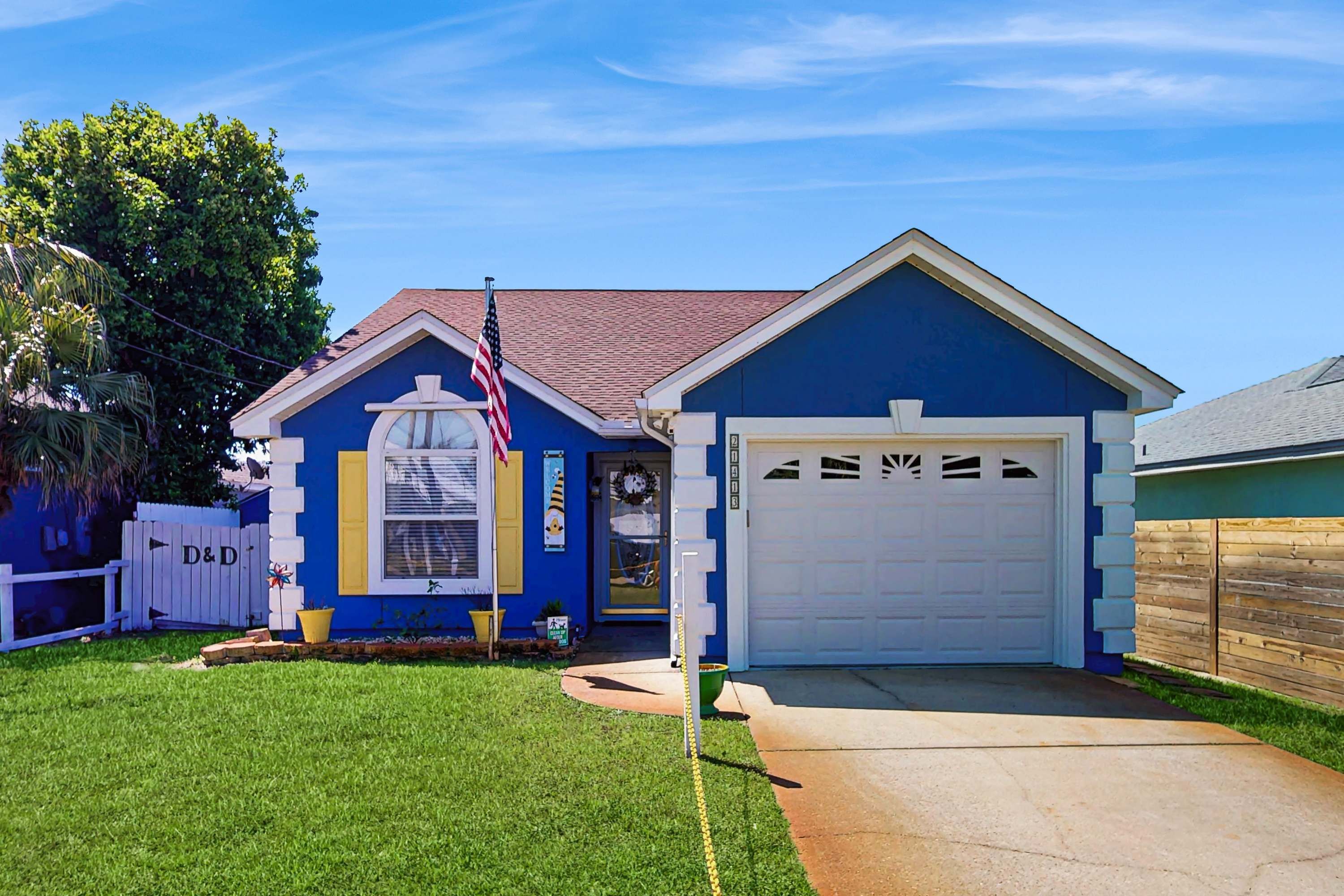 A single-story house with a blue exterior, a white garage door, and a small front yard with a lawn and a mailbox.