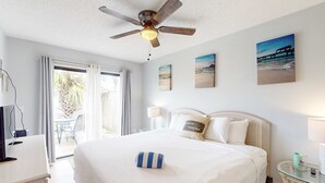 Et hotelværelse med seng, ventilator, fjernsyn, skrivebord, lampe og udsigt til det fri.
