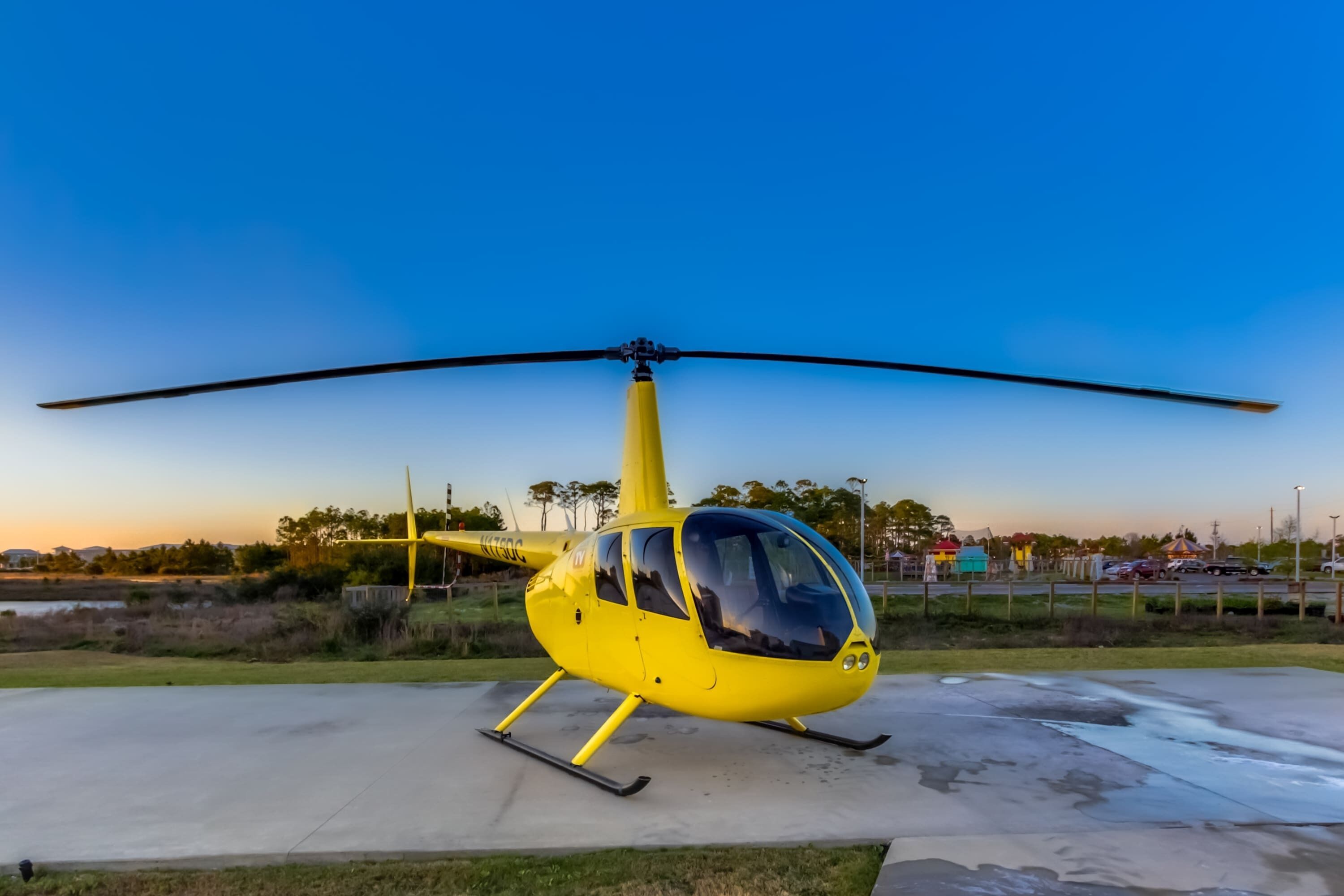 A yellow helicopter parked on a concrete surface.