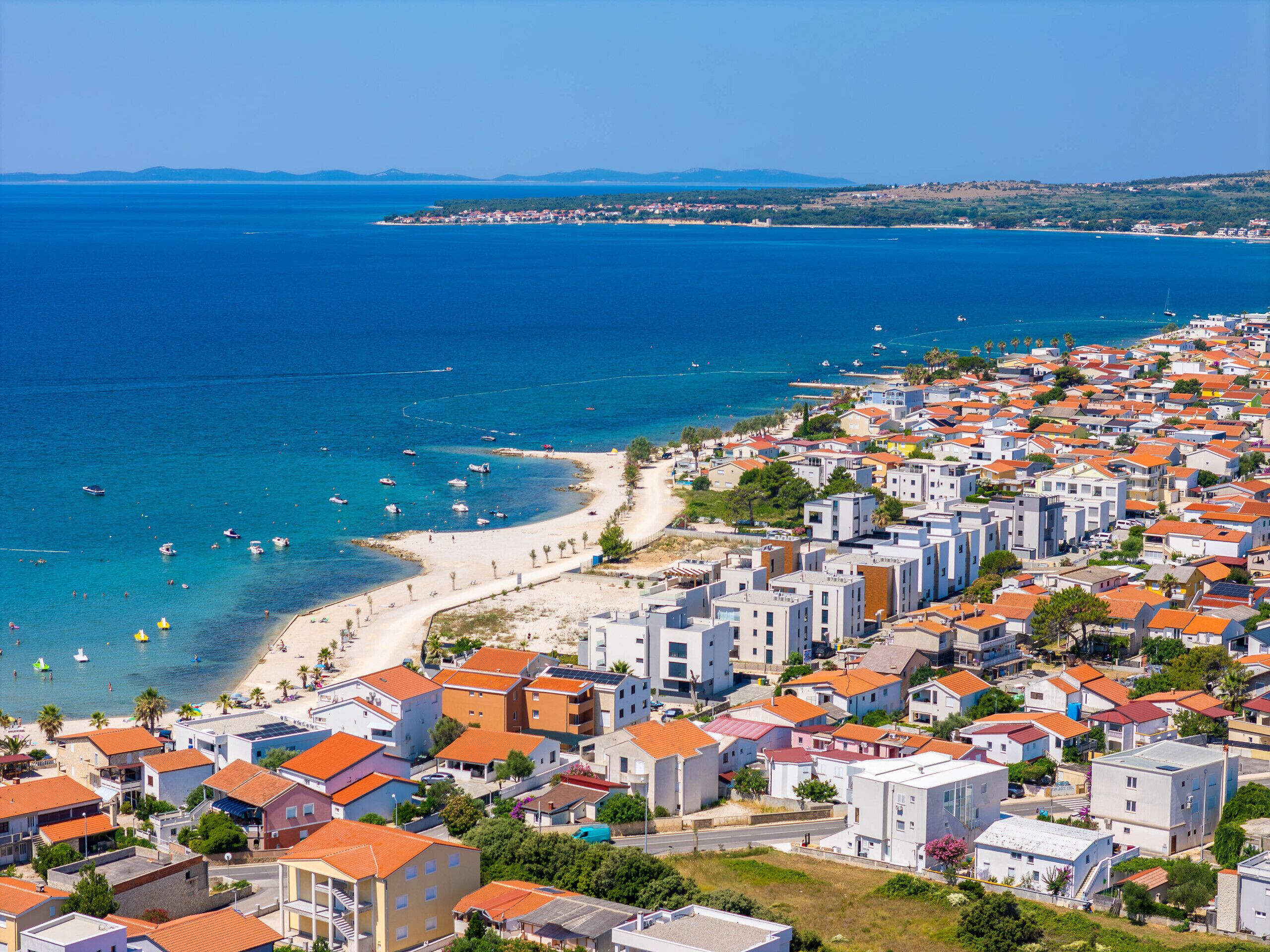 A coastal town with a beach, residential buildings, and boats in the water.