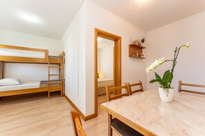 Una stanza con un letto a castello, un tavolo da pranzo con sedie, un vaso di fiori e uno specchio appeso al muro.