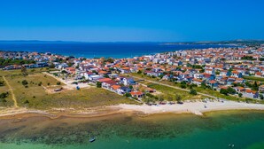 Vista aerea di una cittadina costiera con edifici residenziali, una spiaggia e acque blu cristalline.