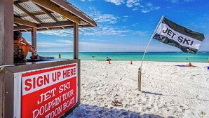 A beach with a Jet Ski sign and a sign-up area for a Dolphin Tour. - Beach condo with WiFi, amazing views, hot tub, and pools (Panama City Beach)