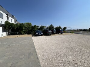 A parking area with three cars parked in a row, a paved walkway, and a building with a white facade and air conditioning units. - Apartment Lavaran 5 (Vir)