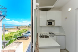 A compact kitchen with a sink, stove, and microwave, a white cabinet, and a view of parked cars and greenery outside. - Apartment Lavaran 5 (Vir)