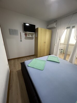 A hotel room with a bed, a television mounted on the wall, an air conditioning unit, and a window with curtains. - Apartment Lavaran 5 (Vir)