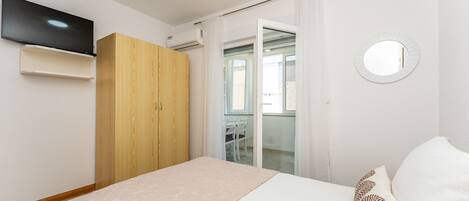 Une chambre à coucher comprenant un lit, une armoire, un téléviseur et une salle de bain visible à travers une porte en verre.