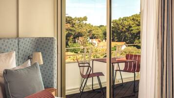 Habitación de hotel con cama, cabecera azul estampada, balcón con sillas y vistas a árboles y casas.