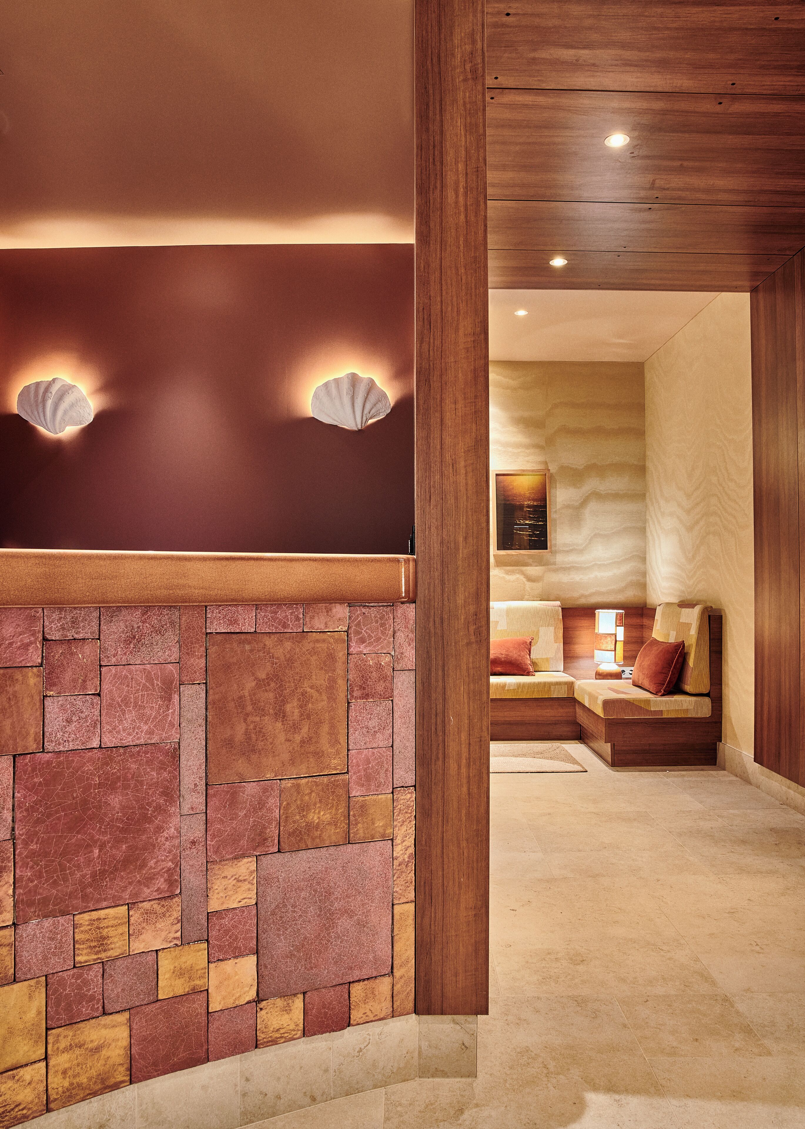 Een hotel lobby met een stenen muur, houten lambrisering en een zithoek met een bank en kussens.