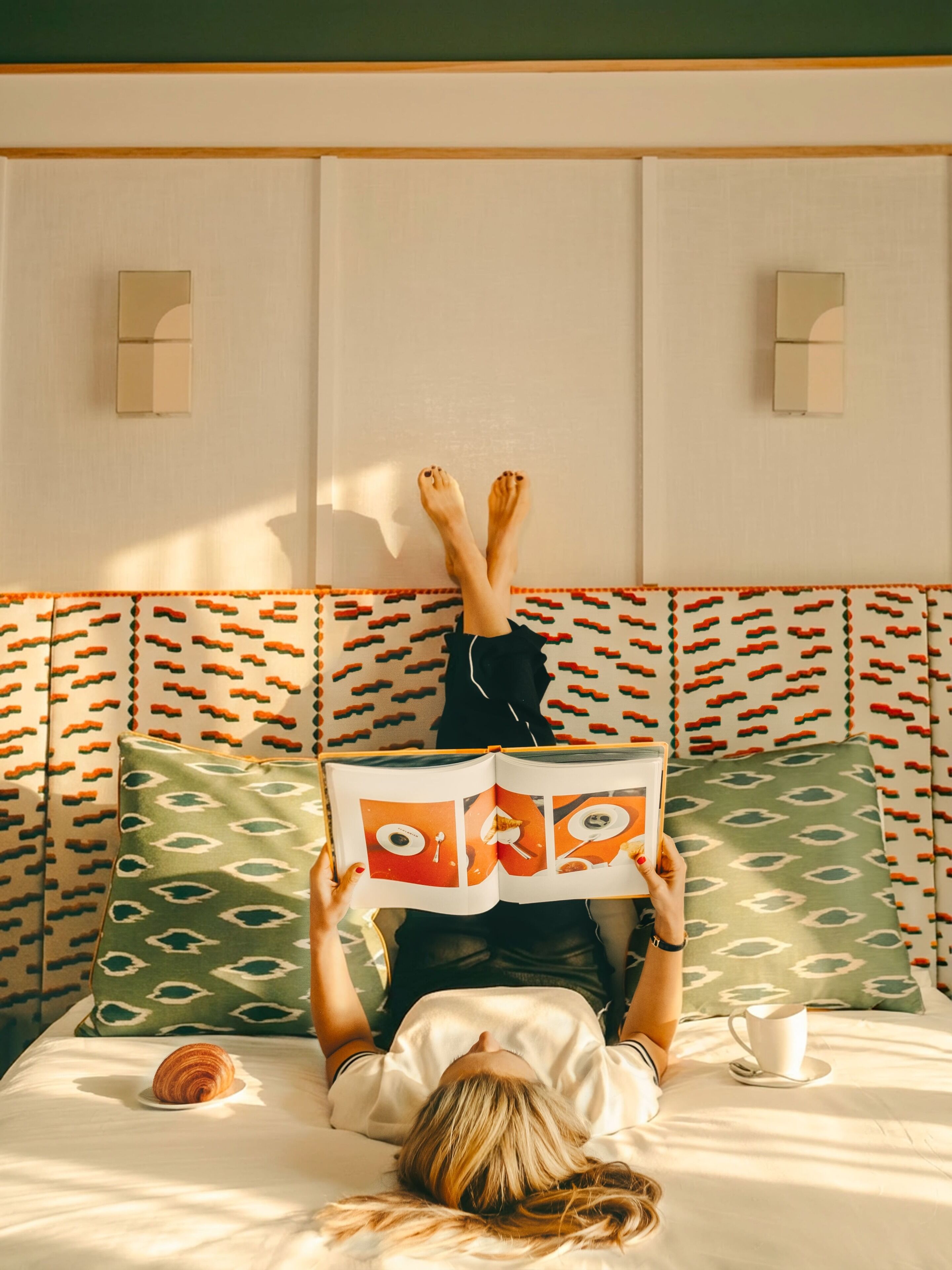 Una persona acostada en una cama con un cabecero estampado, leyendo un libro.