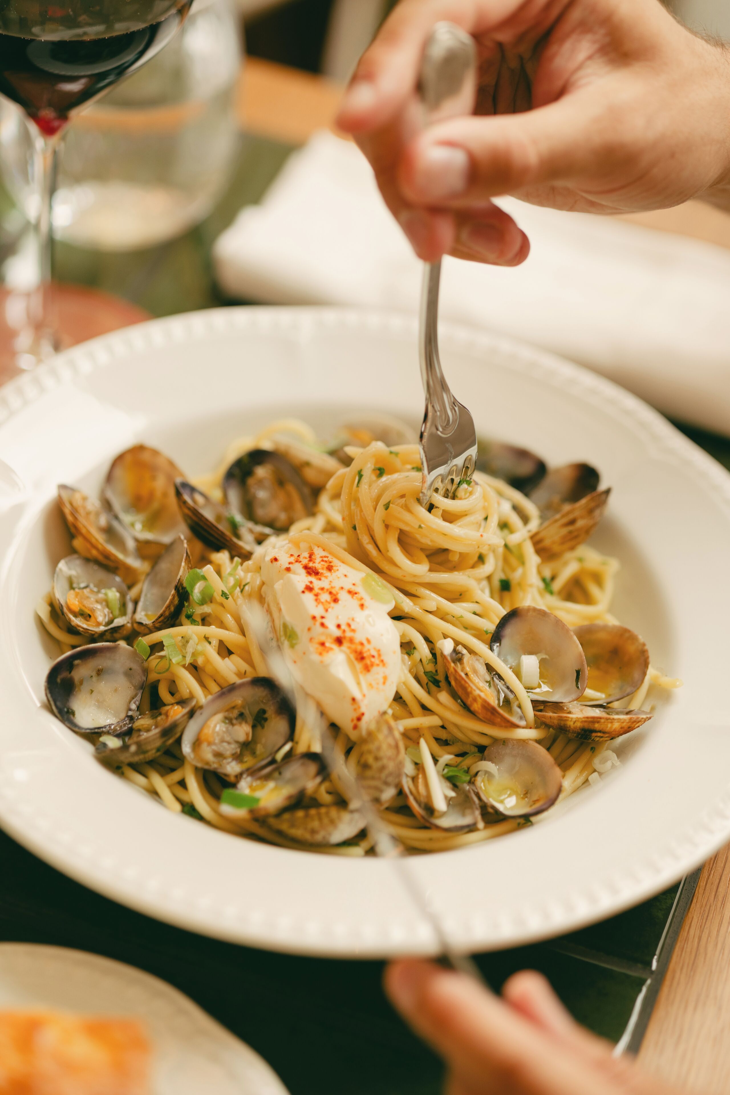 A plate of pasta with clams and a white fish, being eaten with a fork.