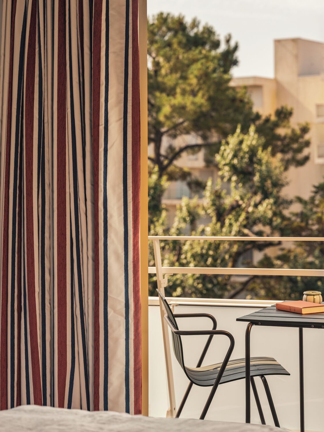 Een balkon met een gestreepte gordijn, een stoel, een tafel en een boek.