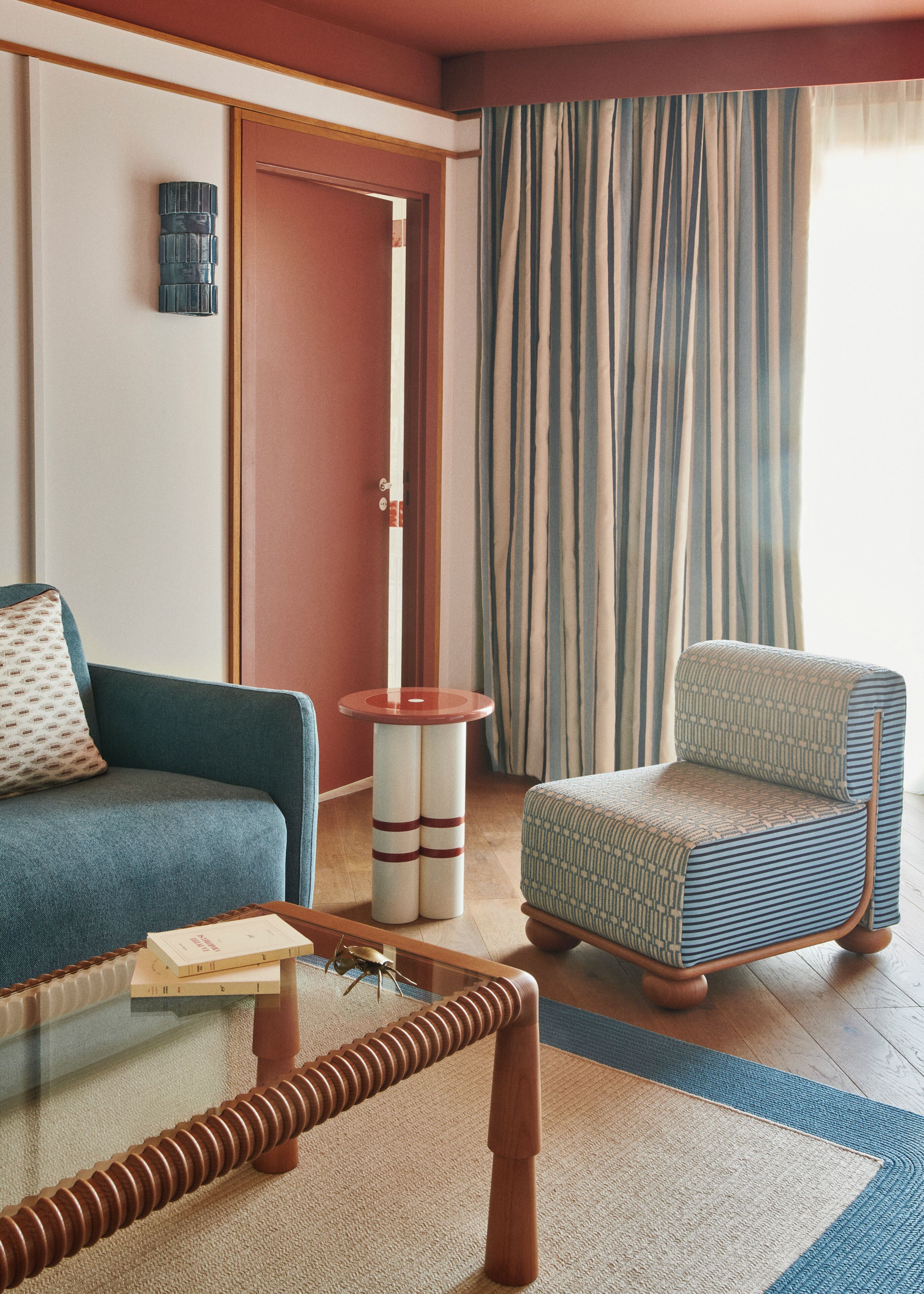 A room with a sofa, armchair, round side table, and a door leading to another room.