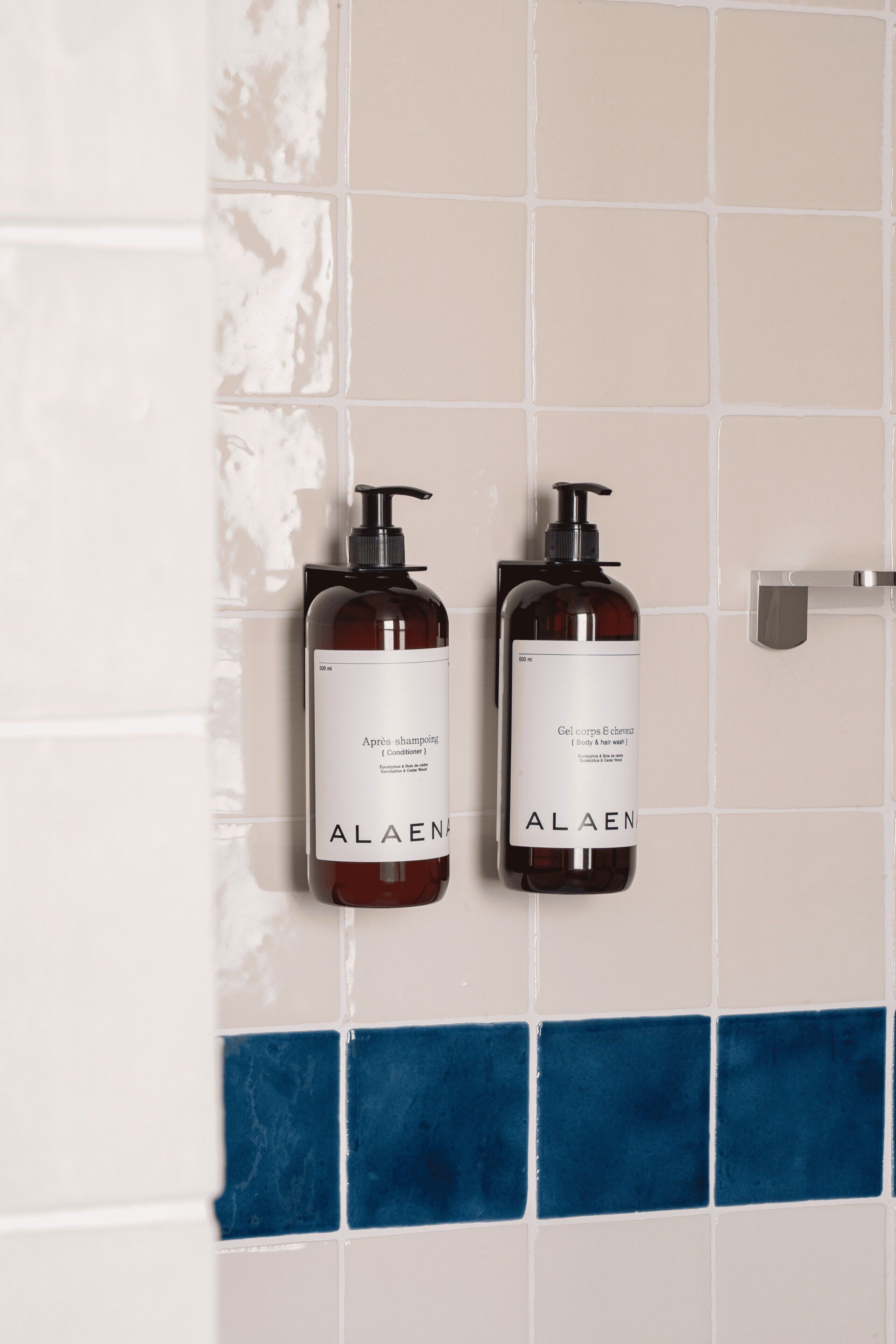 Two bottles of ALAEN body wash on a tiled wall.