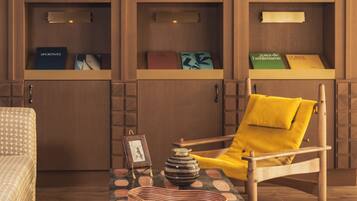 Een kamer met een houten boekenkast, een gele fauteuil, een klein tafeltje met decoratieve objecten en een kamerbreed tapijt met een patroon.